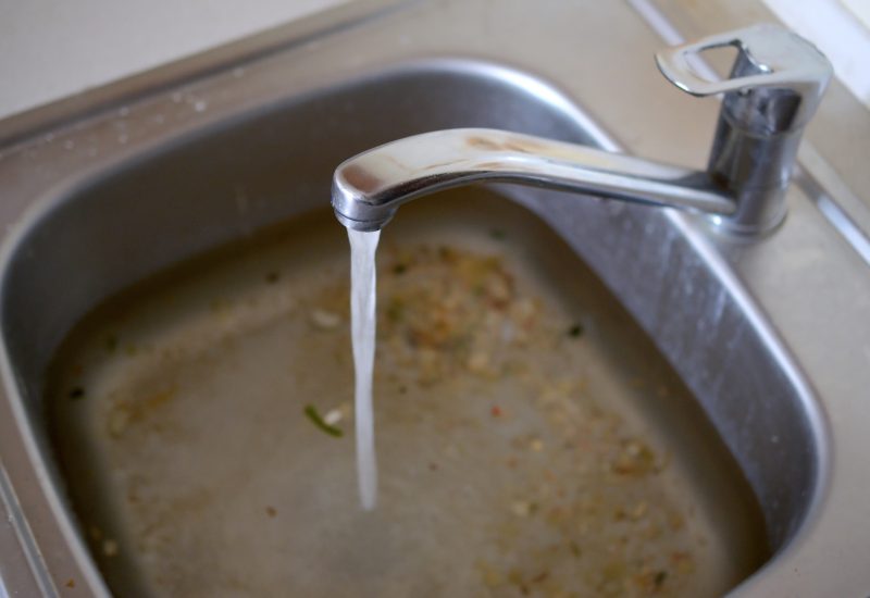Stainless steel sink plug hole close up full of water and particles of food